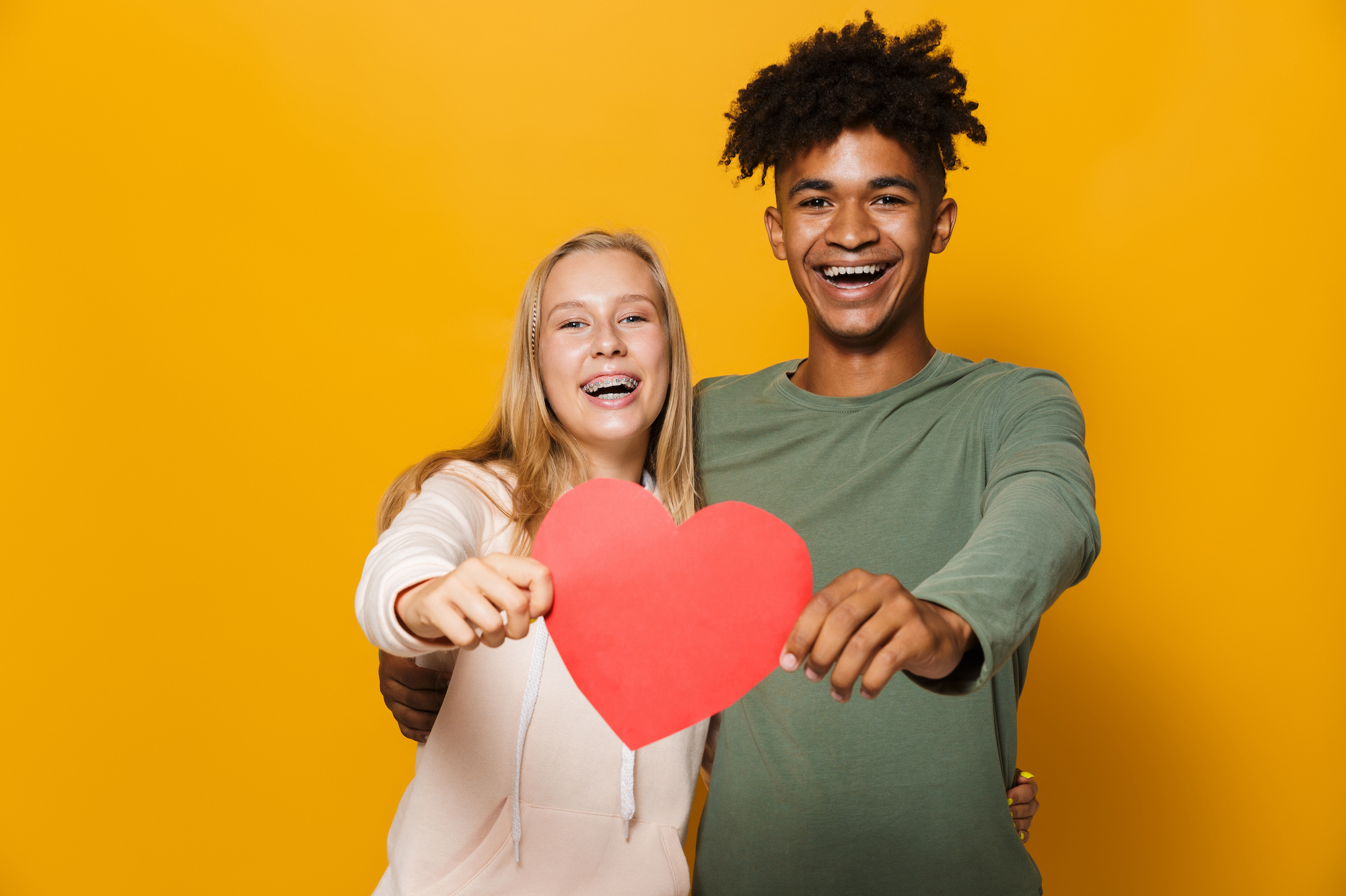 Photo of teenage friends man and woman 16-18 holding paper heart isolated over yellow background